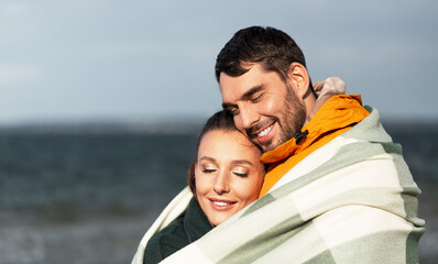 Wall Mural - love, relationship and people concept - happy smiling couple in warm blanket on autumn beach