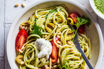 Wall Mural - Spaghetti pasta with pesto sauce, olives, tomatoes and pine nuts in white bowl. Italian cuisine concept.