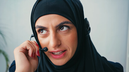 Wall Mural - Muslim woman in hijab using headset and talking in call center