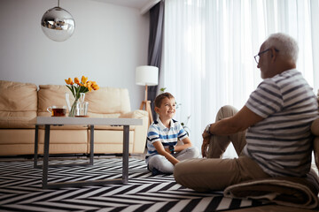 Wall Mural - Happy grandson talks to his grandfather while sitting on the floor at home.