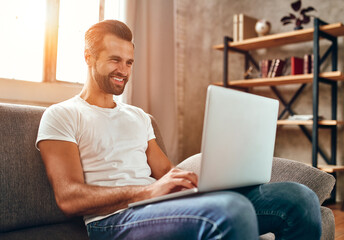 Wall Mural - A man is sitting on the couch with a laptop on his lap. Businessman works online from home. Freelance, communication, online shopping.