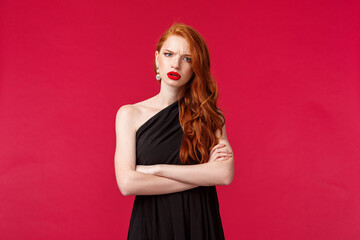 Wall Mural - Portrait of serious and concerned, displeased young redhead woman in black dress, cross hands chest, frowning at camera wtih accusation and judgement, listening to something frustrating