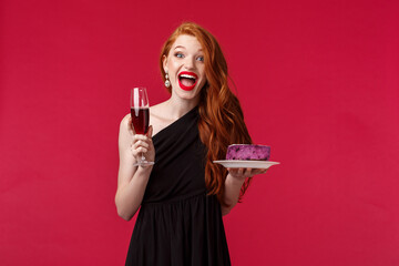 Wall Mural - Portrait of gorgeous festive and excited woman celebrating birthday, feel amused and happy, holding glass champagne and b-day cake, having fun, wear black elegant dress over red background