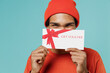 Close up young fun happy african american man 20s wearing orange shirt hat hold cover mouth with gift certificate coupon voucher card for store isolated on plain pastel light blue background studio