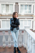 Full Length Of Pensive Young Woman In Black Leather Jacket Standing On Urban Street In Europe