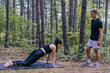 An attractive female athlete is stretching outdoors while her trainer is monitoring her movements