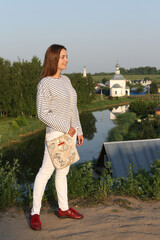 Wall Mural - Russian tourist woman in stripped vest, white jeans in Suzdal town, Russia. Street style, fashion girl. Tourist girl in Suzdal. Suzdal landmark, monument, sightseeing. Summer landscape, Suzdal scenery