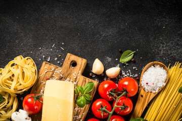 Pasta ingredients on black background. Raw Pasta, parmesan, fresh tomatoes and basil. Top view with copy space.