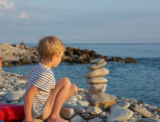 the rays of the setting sun fall on a boy who is playing on a pebble beach. family vacation at the sea.