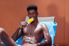 Dark Skinned Man Enjoying A Yellow Popsicle At The Poolside