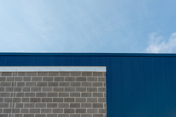 The exterior wall of a commercial building with grey brick, light gray mortar, and silver color flashing or fascia.  There's a deep blue sheet metal siding wall on a high exterior wall above the brick