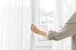 © Pixel-Shot - Young woman opening white curtains at home