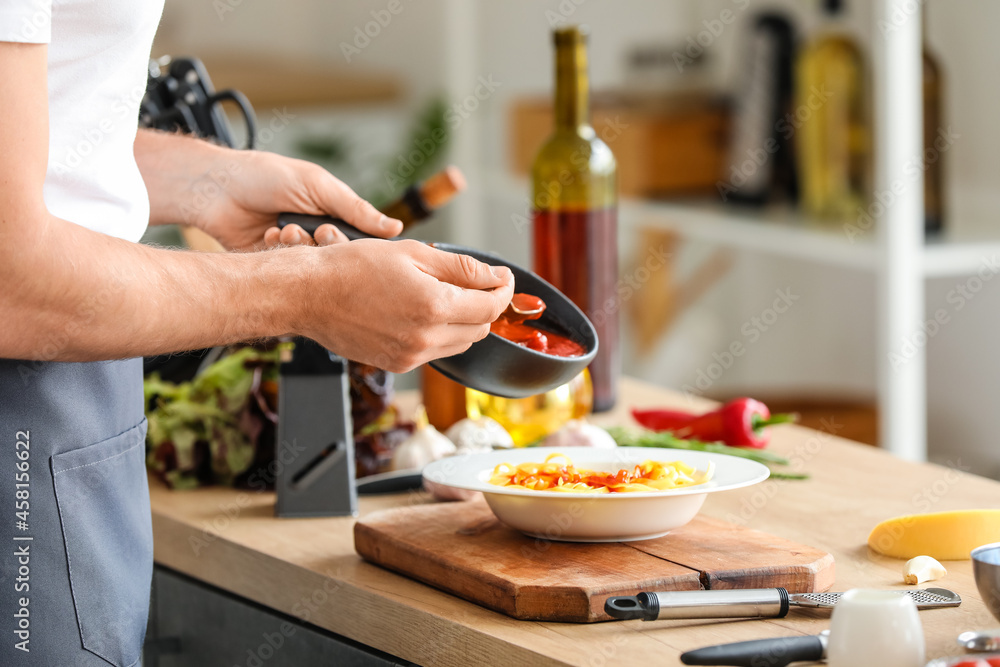 Male chef adding tasty sauce into plate with pasta in kitchen, closeup
