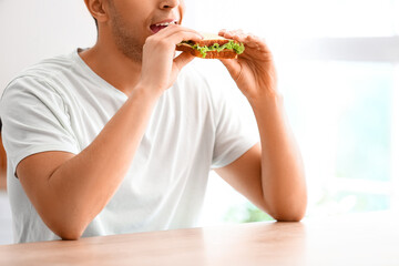 Sticker - Young man eating tasty sandwich in kitchen