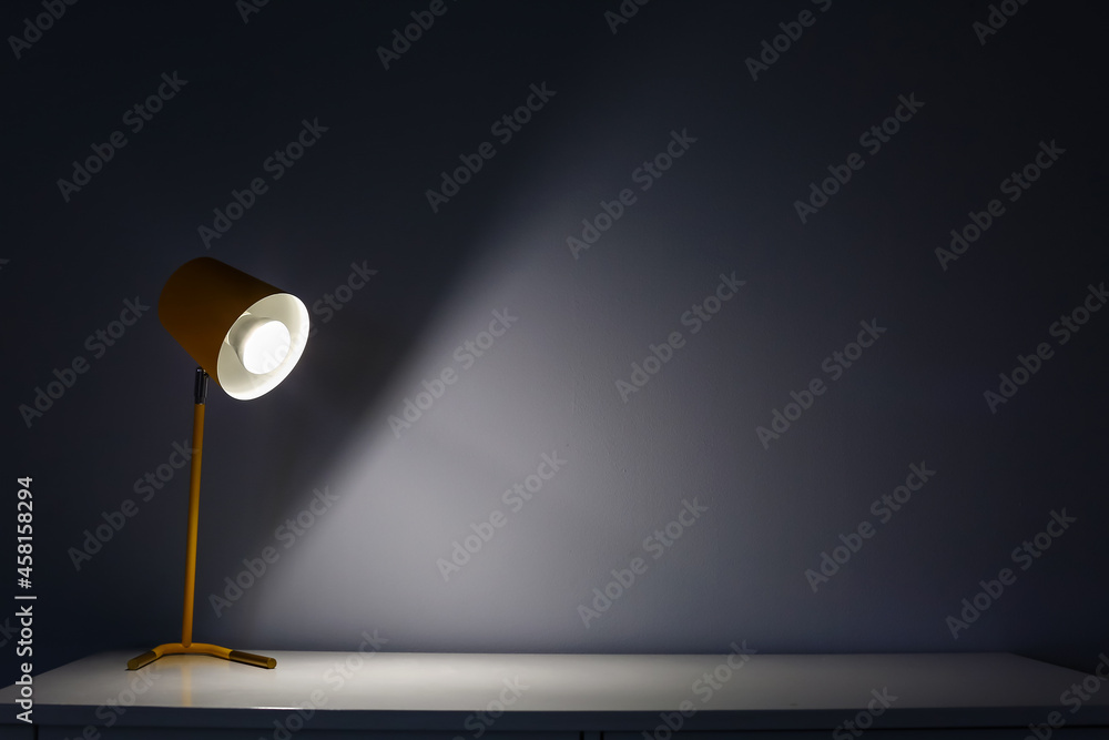 Glowing lamp on table near wall in dark room