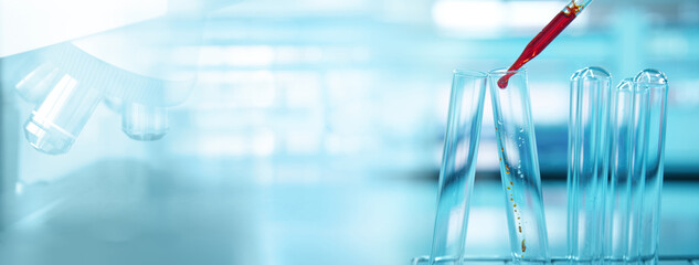 Wall Mural - orange drop in glass test tube and microscope in blue light medical science laboratory banner backgr