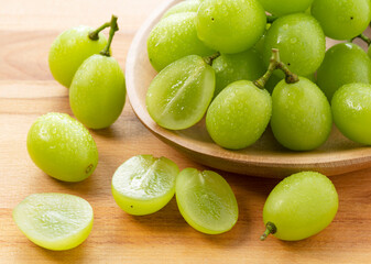 A lot of Shine-Muscat grapes and cut Shine-Muscat grapes on a wooden background.