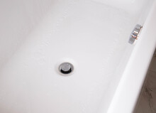 Modern Silver Drain Plug In A New Bathroom, Water Droplets On The Walls Of The Bathtub. Copy Space For Text
