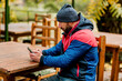 © Sviatlana - A young man using a mobile phone is sitting outdoors in a cafe or restaurant on an autumn day