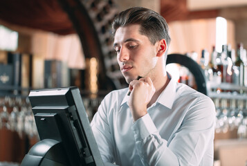 small business, people and service concept - happy man or waiter in apron at counter with cashbox working at bar or coffee shop.