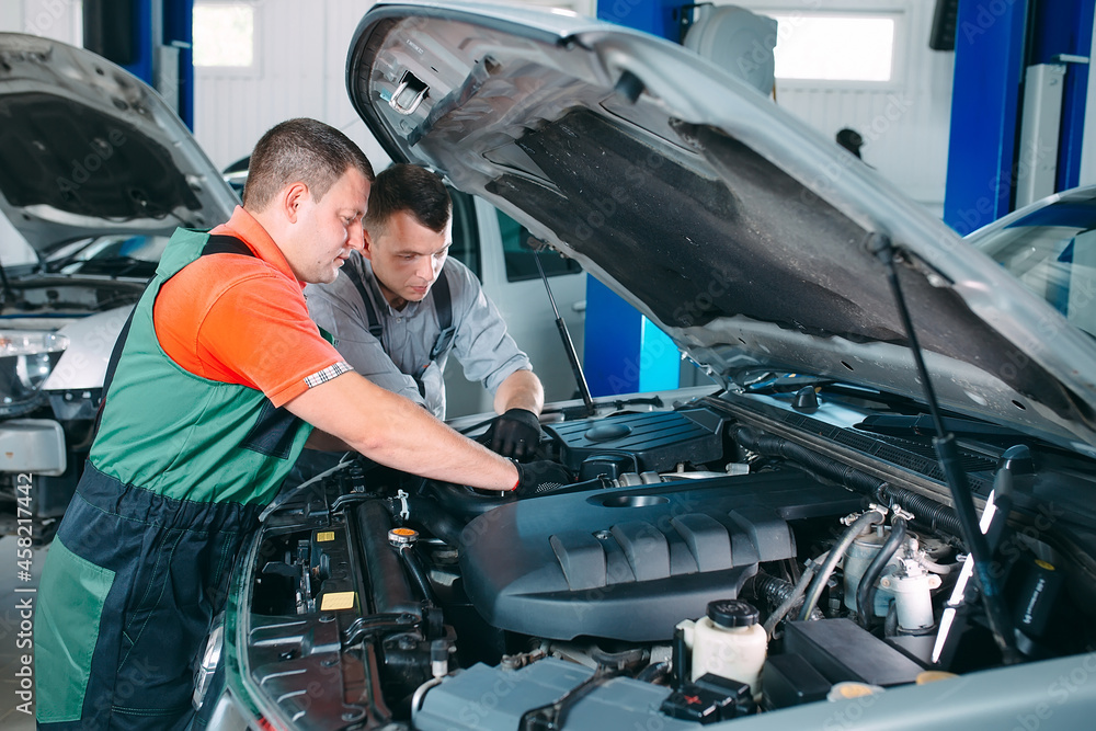 Two handsome mechanics in uniform are working in auto service. Car repair and maintenance.