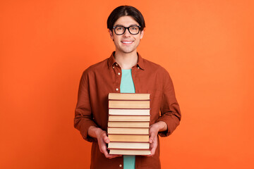 Sticker - Photo of smiling good mood smart intelligent guy hold pile books college students isolated on orange color background