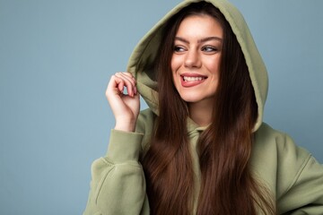 Sticker - Portrait of young beautiful smiling girl in stylish hipster green hoodie. Sexy carefree woman posing near blue wall. Positive model having fun