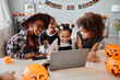 © Seventyfour - Portrait of happy African-American kids wearing Halloween costumes while using laptop at home and video chatting with family online, copy space