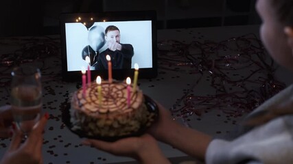 Wall Mural - Online birthday party. Video congratulation. Distance celebration. Happy guy on tablet screen greeting with best wishes female friend blowing candles on cake.