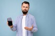 © Ivan Traimak - Closeup Photo of sad dissatisfied handsome good looking young brunette unshaven man with beard wearing casual white t-shirt and blue shirt poising isolated on blue background with empty space holding