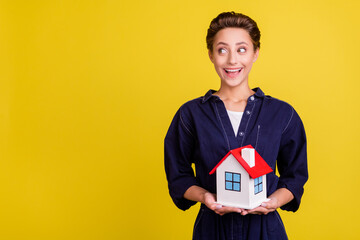 Poster - Portrait of attractive cheerful girl holding in hand house flat copy space ad isolated over vibrant yellow color background