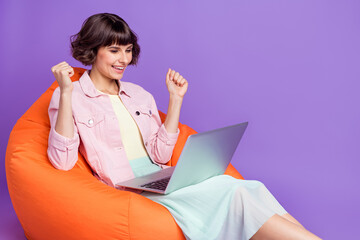 Sticker - Photo of happy cheerful young woman winner hold hand computer good mood sit chair isolated on violet color background