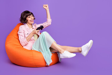 Sticker - Full size photo of young cheerful woman sit bean bag chair winner gamer race isolated on purple color background