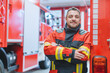Experienced fire fighter man standing in front of fire truck with arms crossed