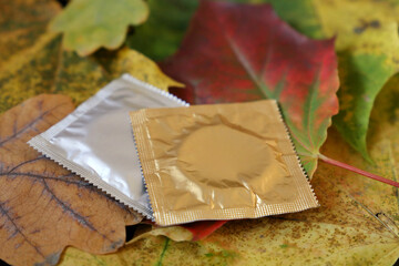 Condom packages on orange and yellow maple and oak leaves. Contraception, safety sex in autumn season