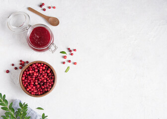 Concept flat lay with homemade lingonberry jam and forest cowberry in bowl on white table with blue napkin.   Top view and copy space