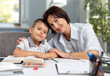 © MYDAYcontent - Happy caucasian mother embracing her lovely son while sitting together at desk with books and notes. Domestic studying and family time concept.