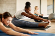 © Drazen - African American athletic woman stretches during group workout at gym.