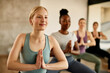 © Drazen - Smiling athletic woman practices Yoga with hands clasped during exercise class at health club.