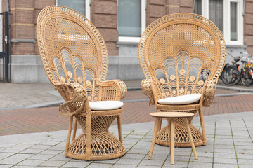 Two rattan wicker chairs in peacock shape and boho, hippie, eclectic home decor style standing outside at a cafe in the Netherlands