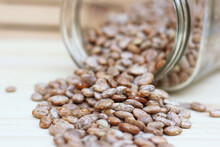 Selective Focus Shot Of Pinto Beans Spilled On A Wooden Kitchen Table From A Glass Jar