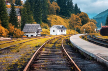 Railway Station And Small White House In Mountain Village In Autumn In Europe. Rural Railroad In Fall. Industrial Landscape With Railway Platform, Orange Trees And Grass, Buildings. Transportation