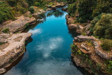 Wall Mural - Beautiful view of the water surrounded by rocks, stones, trees, plants on a sunny day