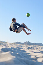 Vertical Shot Of A Young Male Jumping On A Beach For A Ball