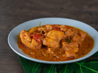 Wall Mural - Ayam Kapitan (Kapitan Chicken), Malaysian Curry close up on dark background with copy space. Spicy Asian curry with coconut gravy and chili on wooden table.