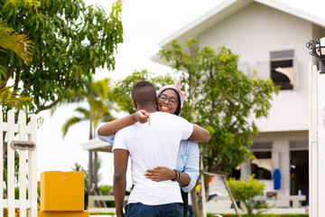 African American wife hugging her husband in front of the house they just move in while holding key for housing, relocation and new family