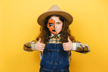 Portrait Of Happy Cute Caucasian Little Girl Kid With Halloween Makeup Mask, Smiling Looking At Camera, Showing Thumbs Up, Posing Isolated On Yellow Color Background Wall. Party Holiday Concept