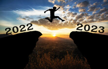 A Young Man Jump Between 2022 And 2023 Years Over The Sun And Through On The Gap Of Hill  Silhouette Evening Colorful Sky. Happy New Year 2022.