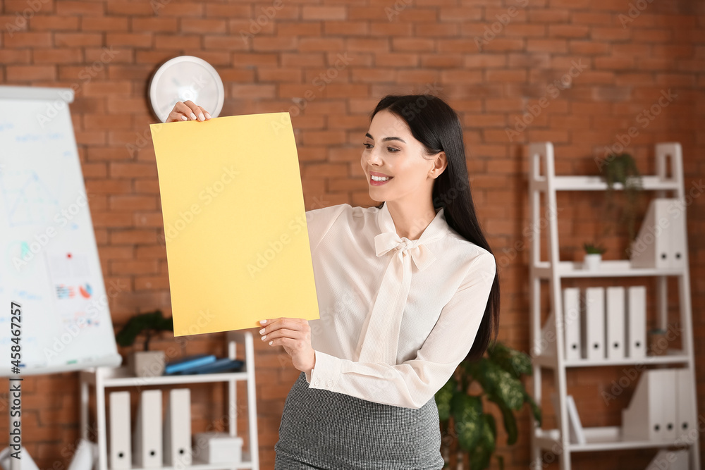 Young woman holding blank paper sheet in office