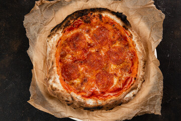 Delicious pizza with tomatoes pepperoni Margarita fresh Pastries on a black concrete background. Top view of a hot pepperoni pizza. With space for text. He was lying flat. Ruddy dough on kraft paper 